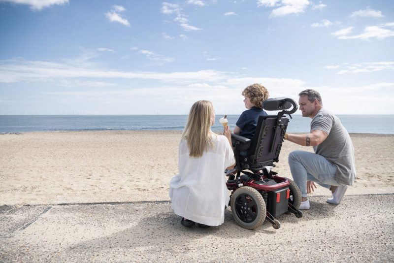 Parents-crouching-by-wheelchair-at-beach